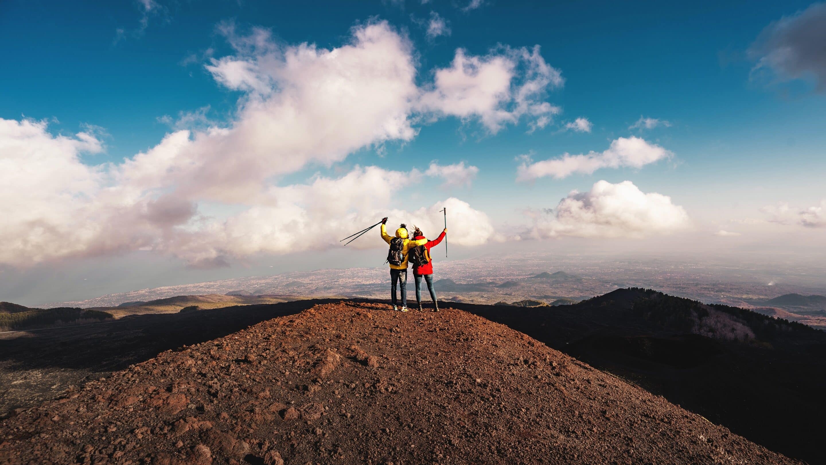 Two hikers stand triumphantly on a volcanic ridge on Mount Etna in Sicily, Italy